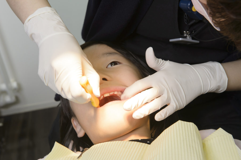 乳歯が抜けず歯医者さんで抜歯する子どものイメージ写真